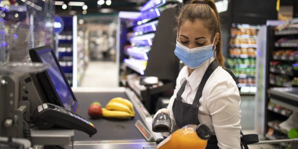 Cashier in supermarket wearing mask and gloves fully protected against corona virus.