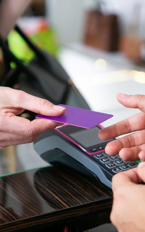 Customer giving credit card to cashier over desk with pos terminal for payment. Cropped shot, closeup of hands. Shopping concept