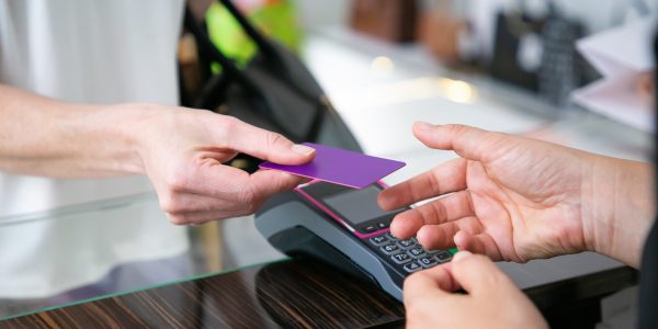 Customer giving credit card to cashier over desk with pos terminal for payment. Cropped shot, closeup of hands. Shopping concept