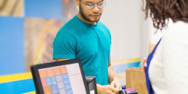 Focused young man paying bill in store. Back view of cashier standing at workplace. Shopping concept