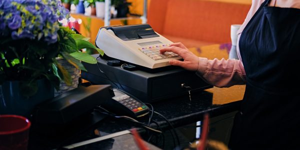Redhead female flower seller using cash register in a market shop.